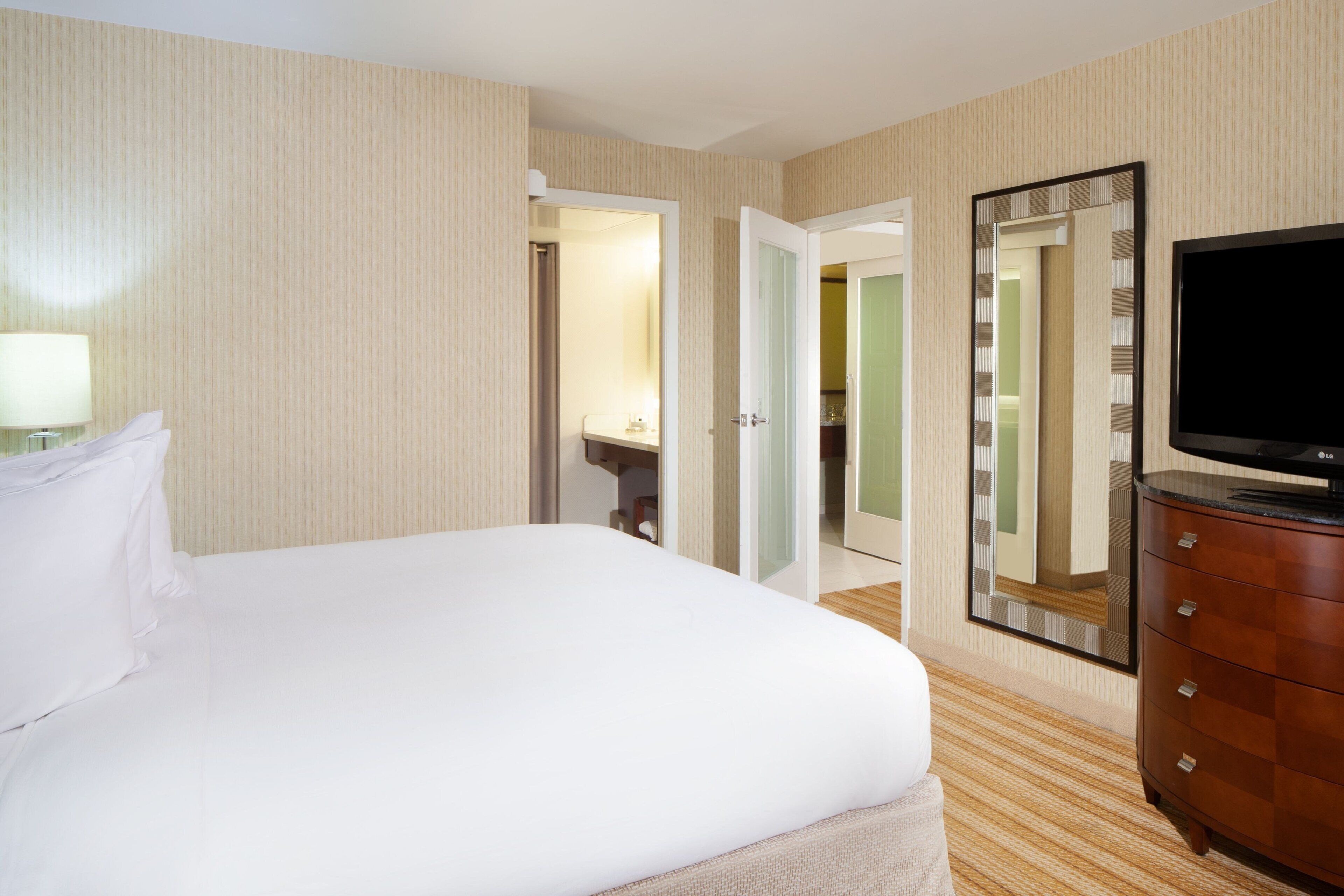 A hotel room with a bed, a dresser, a TV, and a mirror.