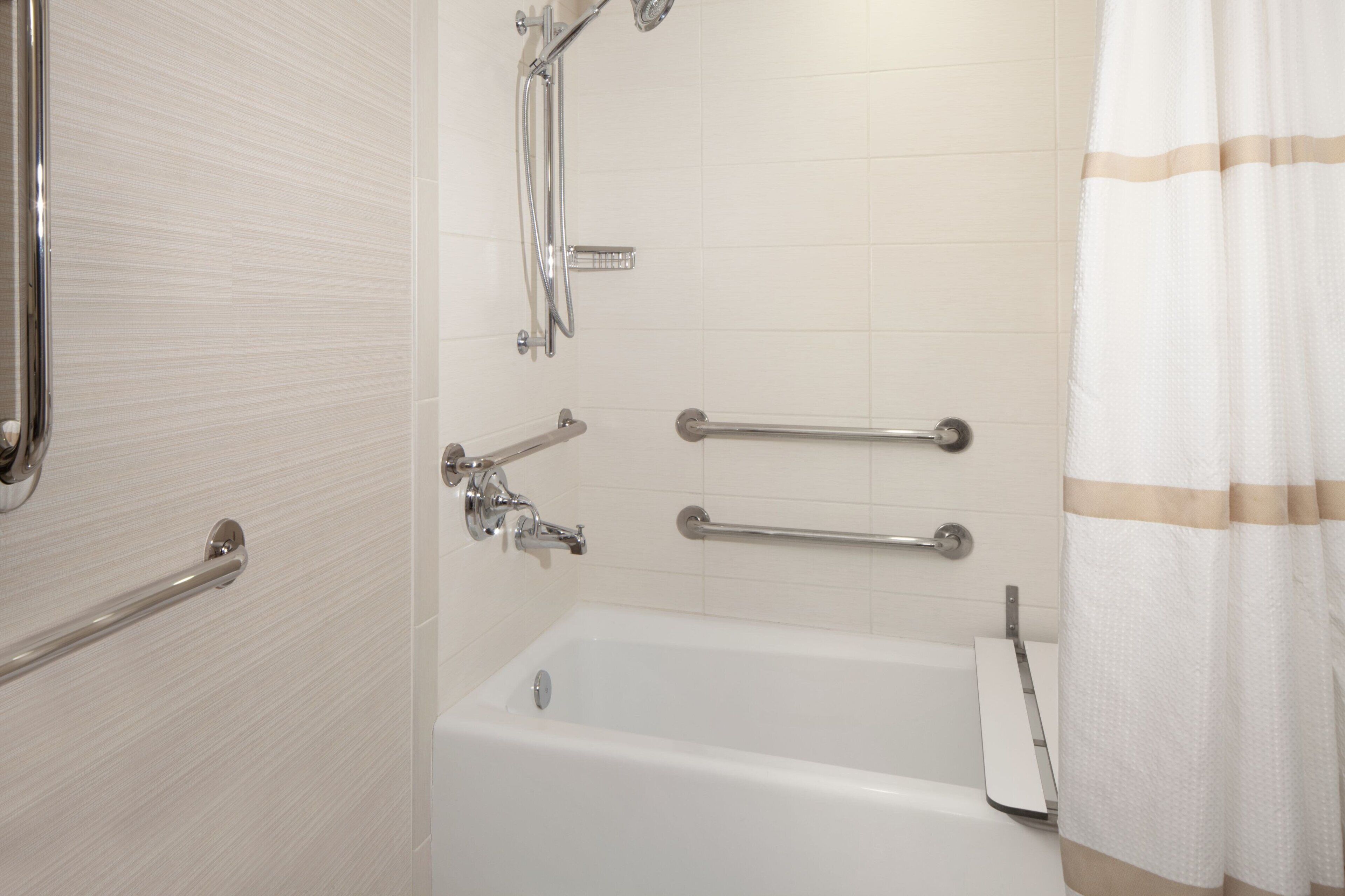 A bathroom with a bathtub, grab bars, and a showerhead.