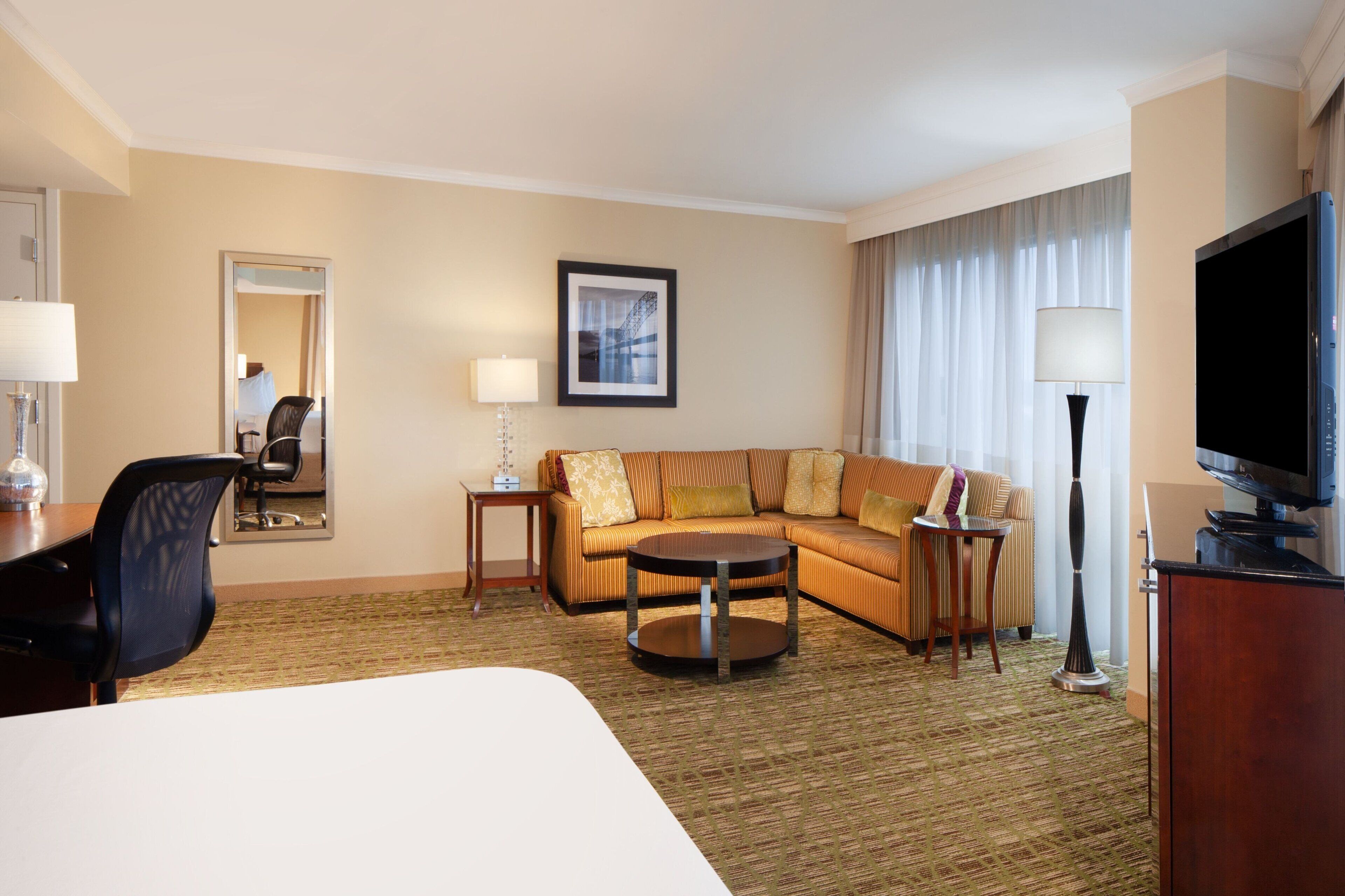 A hotel room with a large bed, a sofa, a coffee table, a TV, and a desk with a lamp.