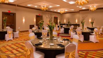 A banquet hall with round tables, white chairs with gold sashes, and floral centerpieces.