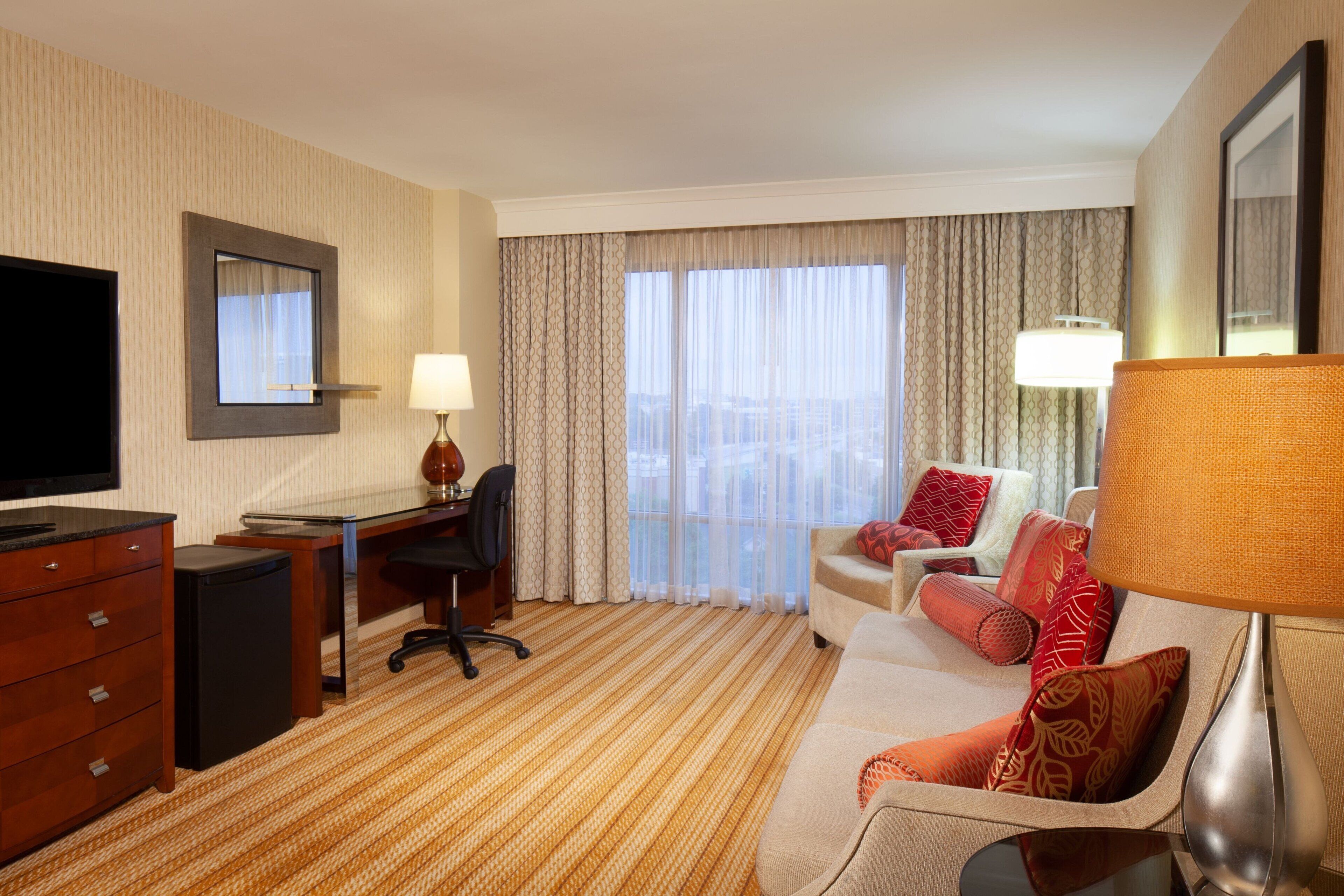 A hotel room with a bed, a desk, a chair, a TV, and a window with curtains.