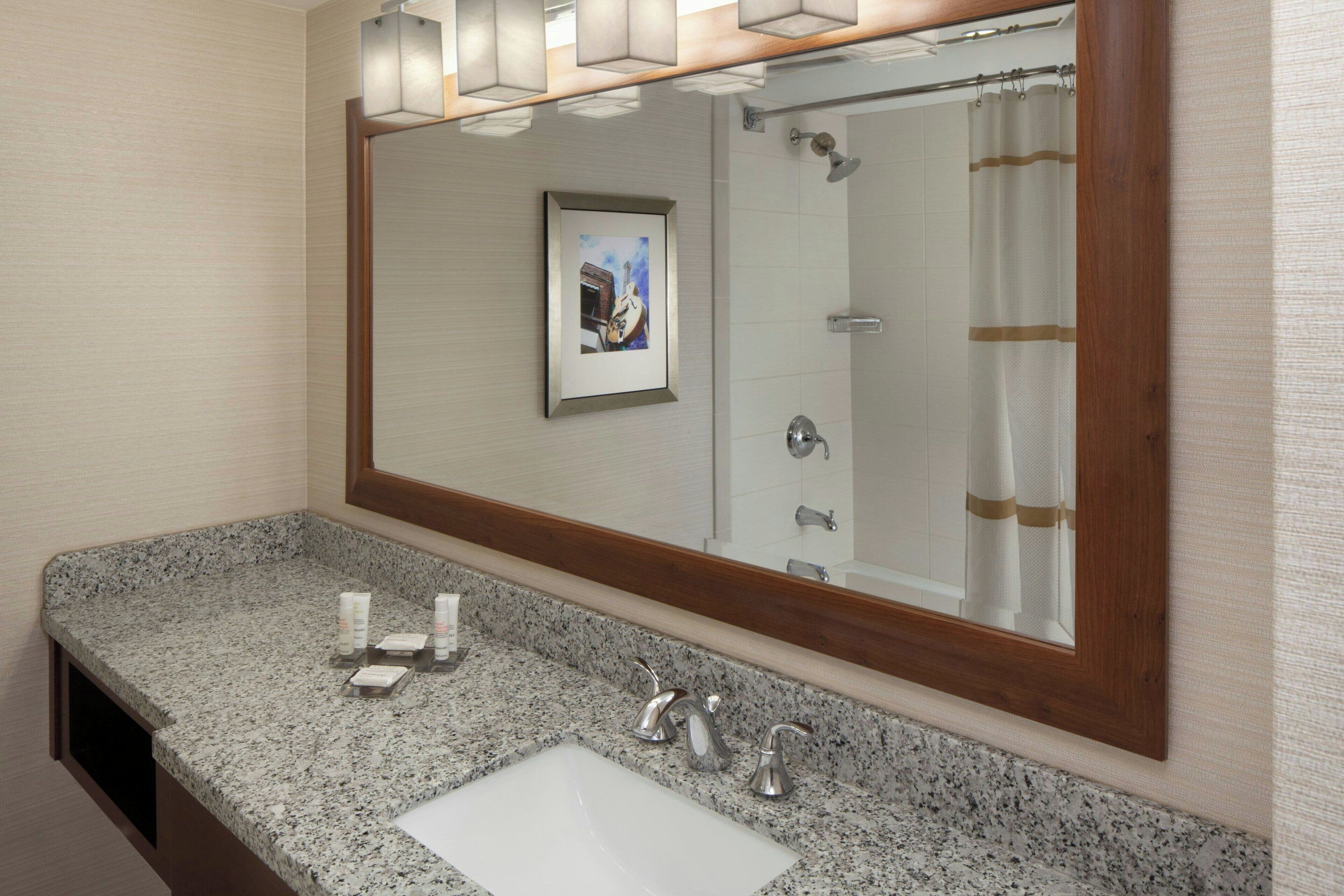 A bathroom with a granite countertop, a white sink, two faucets, a framed mirror, and a shower curtain.