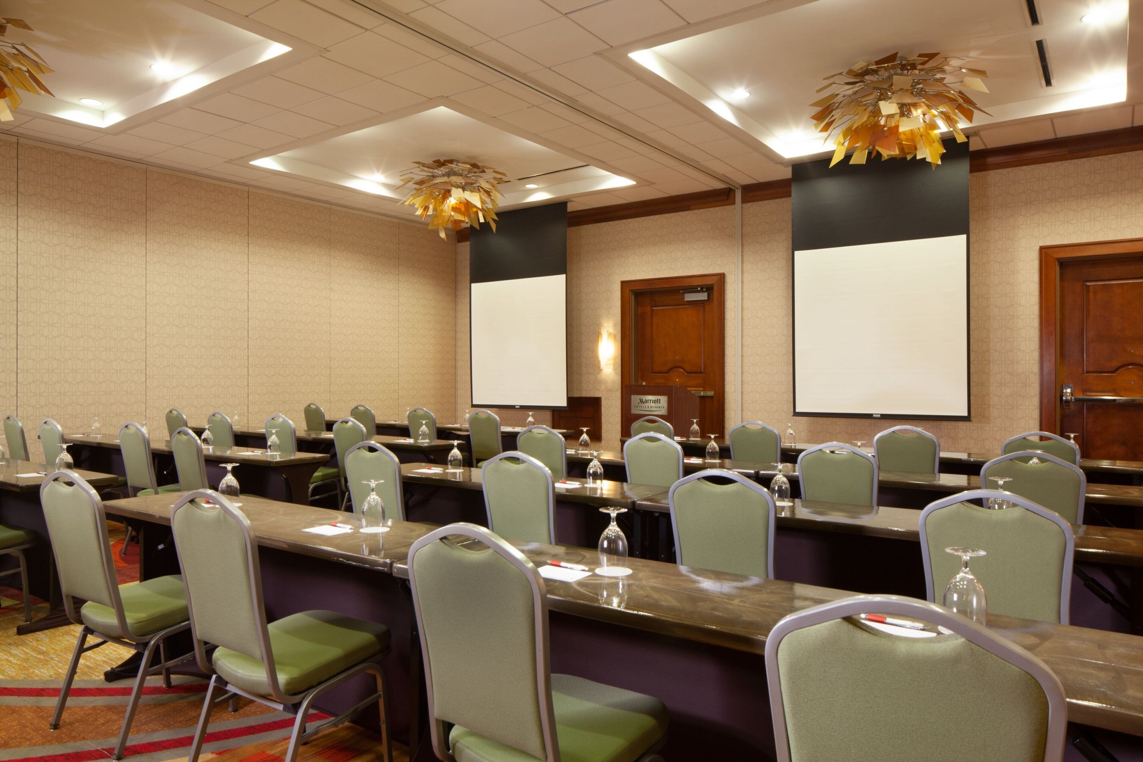 Un salón de conferencias con varias mesas, sillas y una pantalla grande.