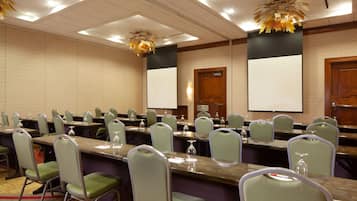 Un salón de conferencias con varias mesas, sillas y una pantalla grande.