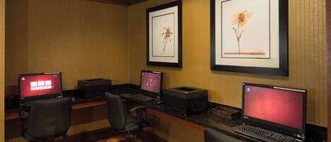 A hotel room with three desktop computers, two office chairs, and framed floral artwork on the wall.