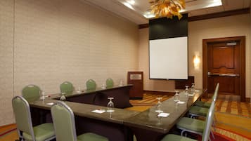 A conference room with a long table, green chairs, a podium, and a projector screen.