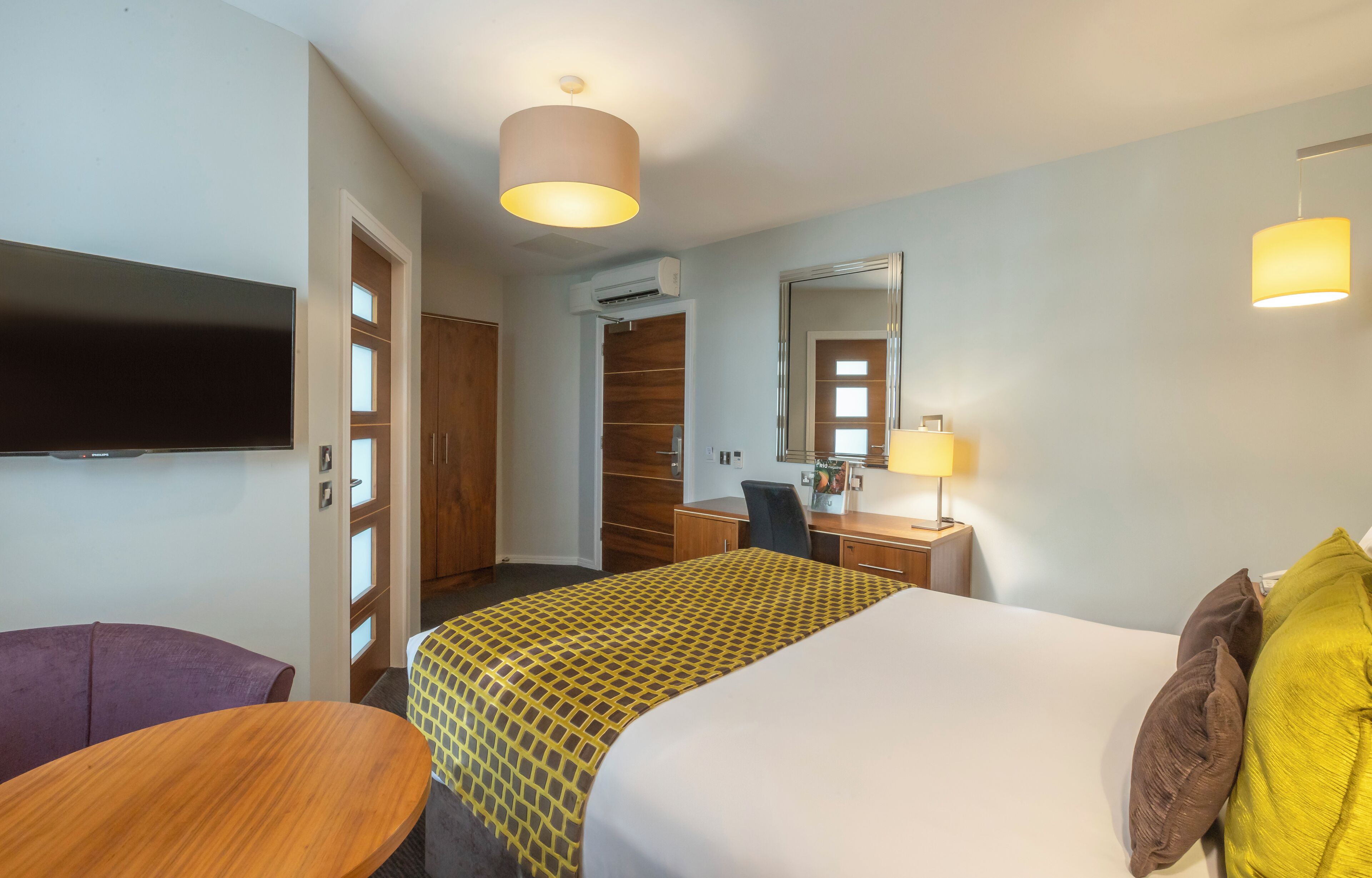 Une chambre d’hôtel comprenant un lit, un bureau, une chaise, une télévision et une armoire.