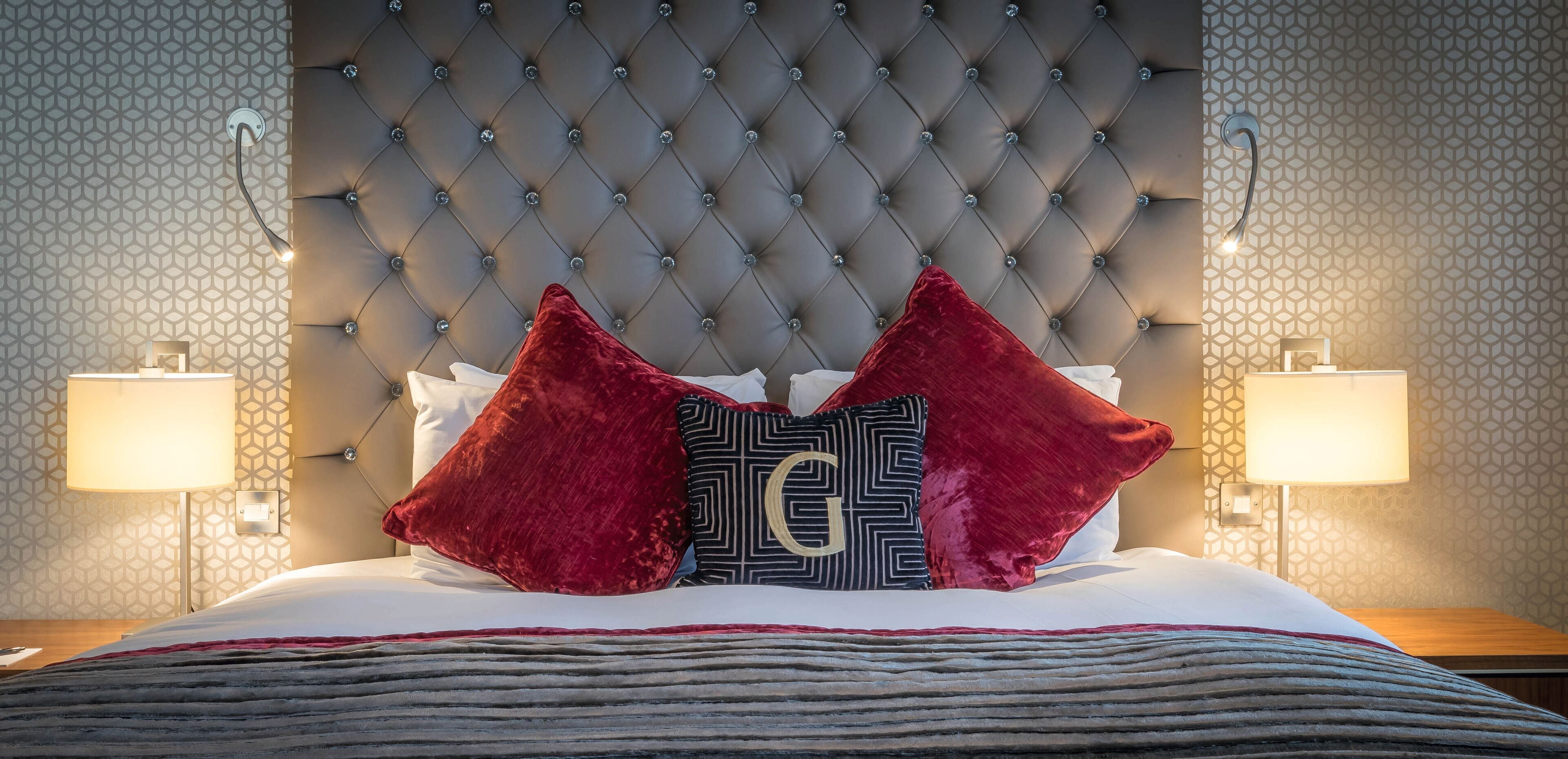 A hotel room with a tufted headboard, two bedside lamps, and a bed with a striped blanket.