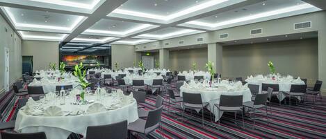 A spacious banquet hall with multiple round tables set for dining, featuring white tablecloths and chairs.
