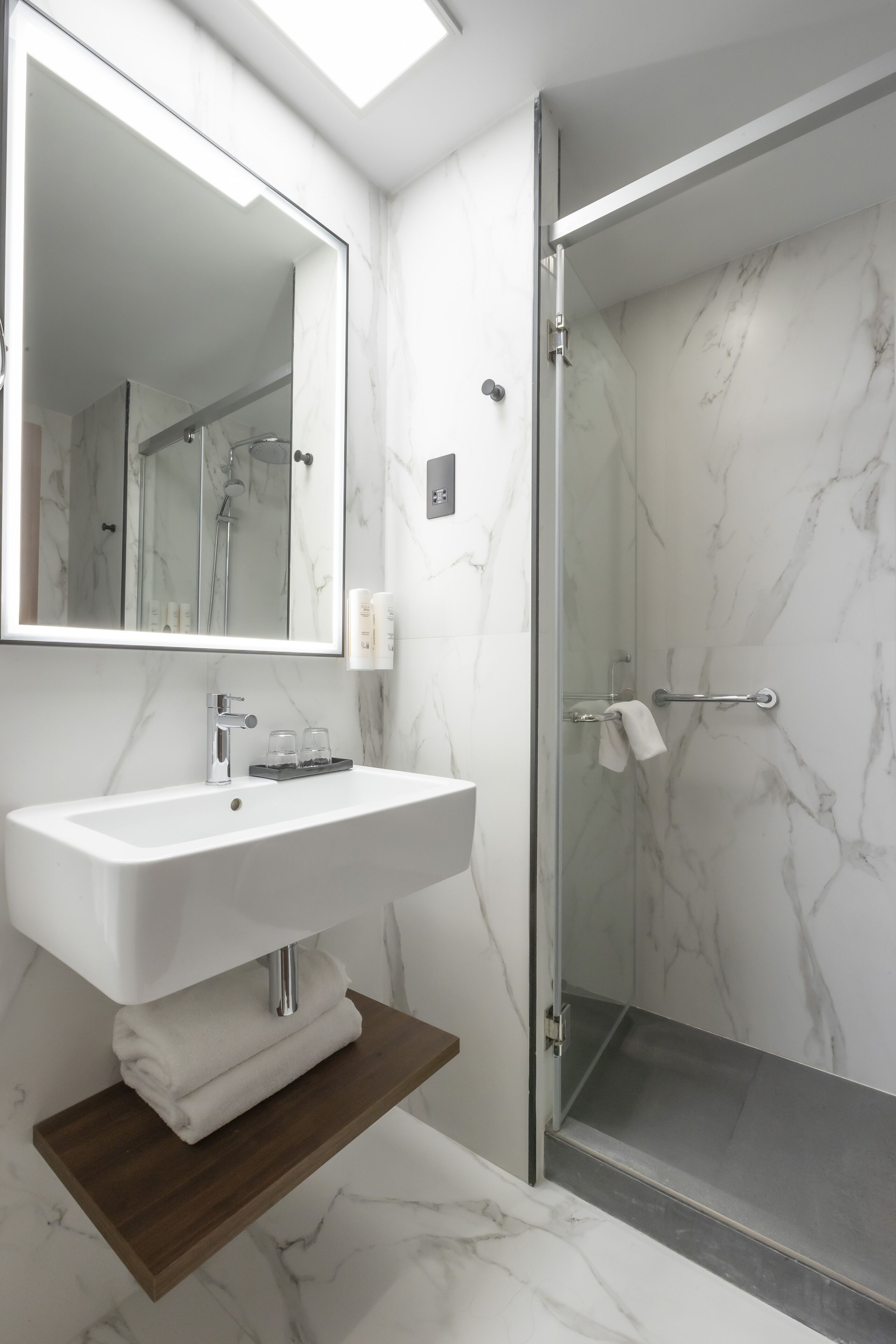Un baño moderno con un lavabo de mármol blanco, un espejo grande y una ducha con paredes de vidrio.
