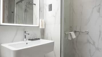Un baño moderno con un lavabo de mármol blanco, un espejo grande y una ducha con paredes de vidrio.