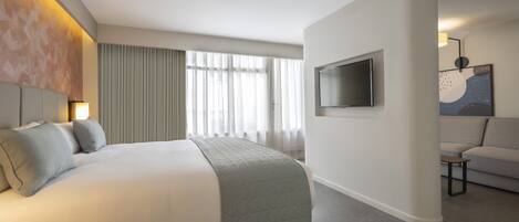 A hotel room with a bed, a TV, a sofa, and a large window with curtains.