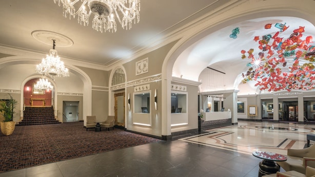 A spacious lobby with a grand chandelier, a reception desk, and a large, colorful sculpture.