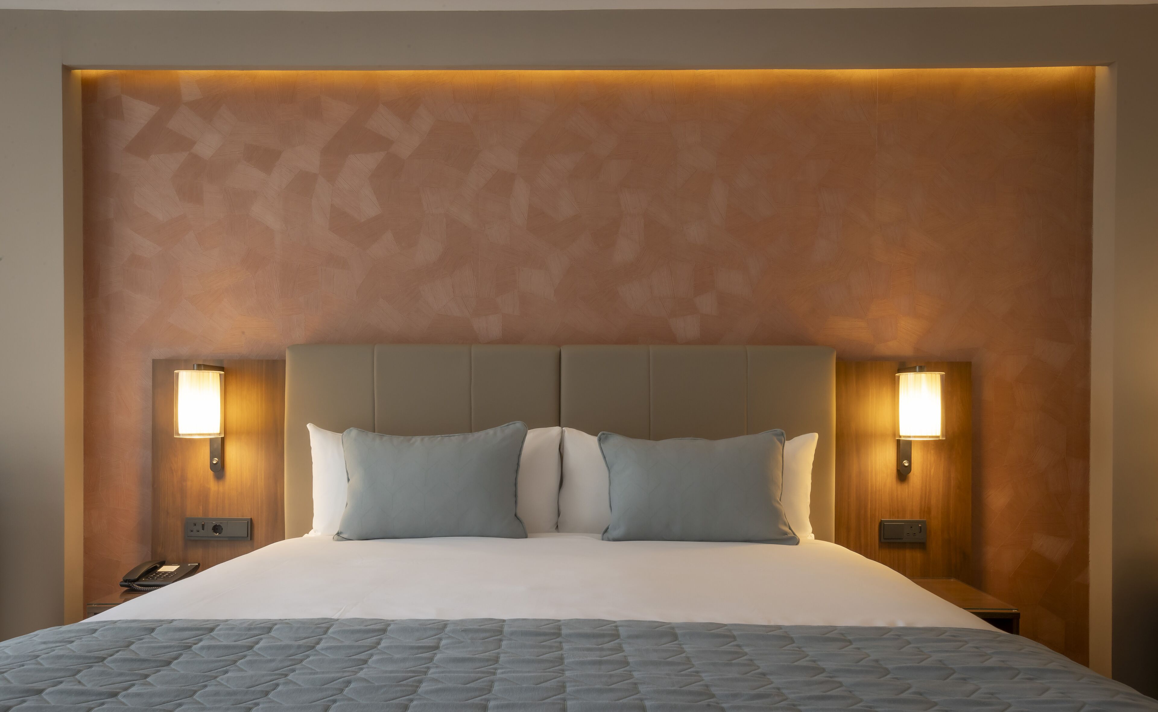 A neatly made bed with a quilted cover, two bedside lamps, and a wooden headboard.
