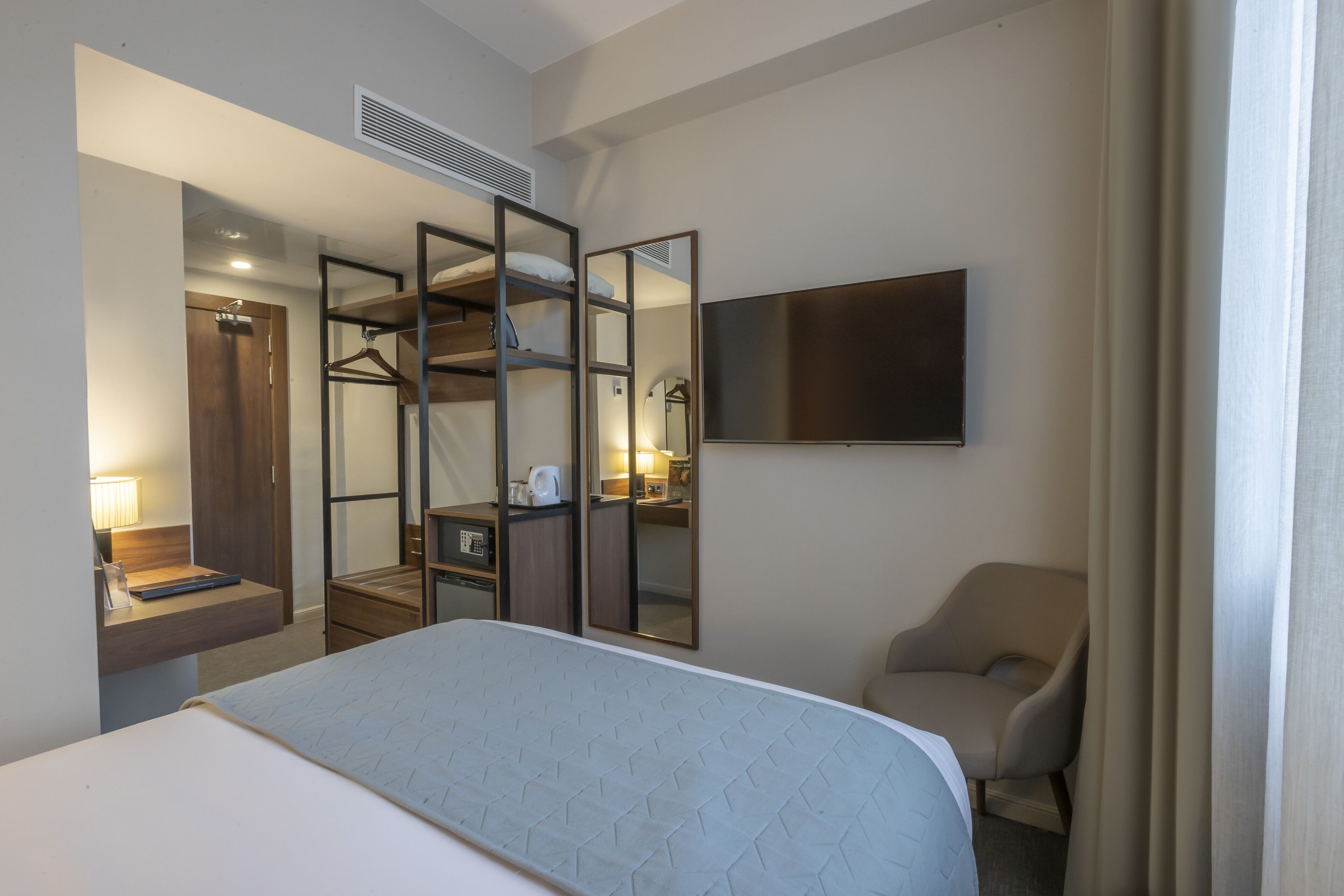 A hotel room with a bed, a chair, a TV, a mirror, and a wardrobe.