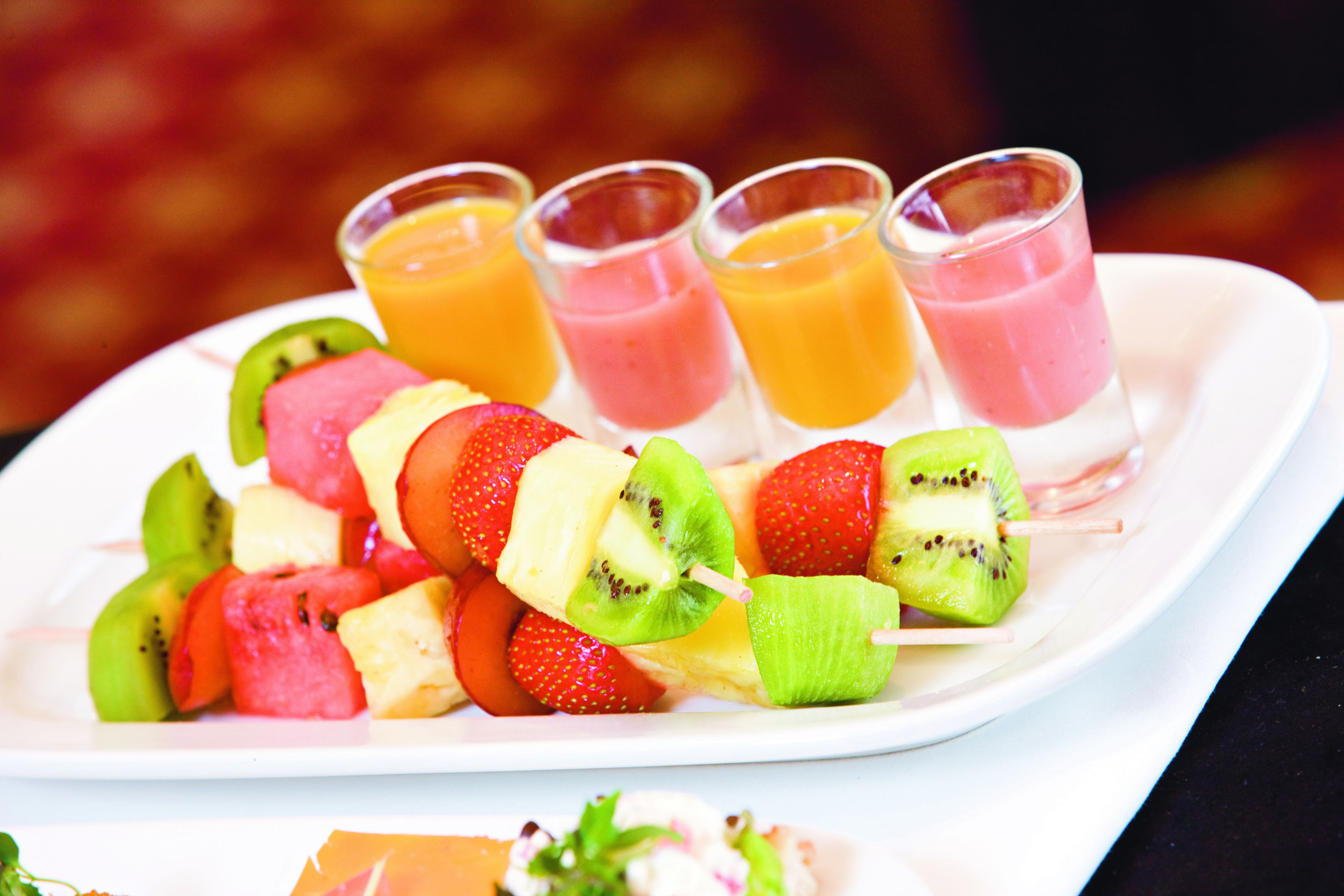 A plate with fruit skewers and four fruit juices.