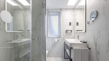 A modern bathroom with a glass shower enclosure, a white sink with a mirror, and a marble-tiled wall.