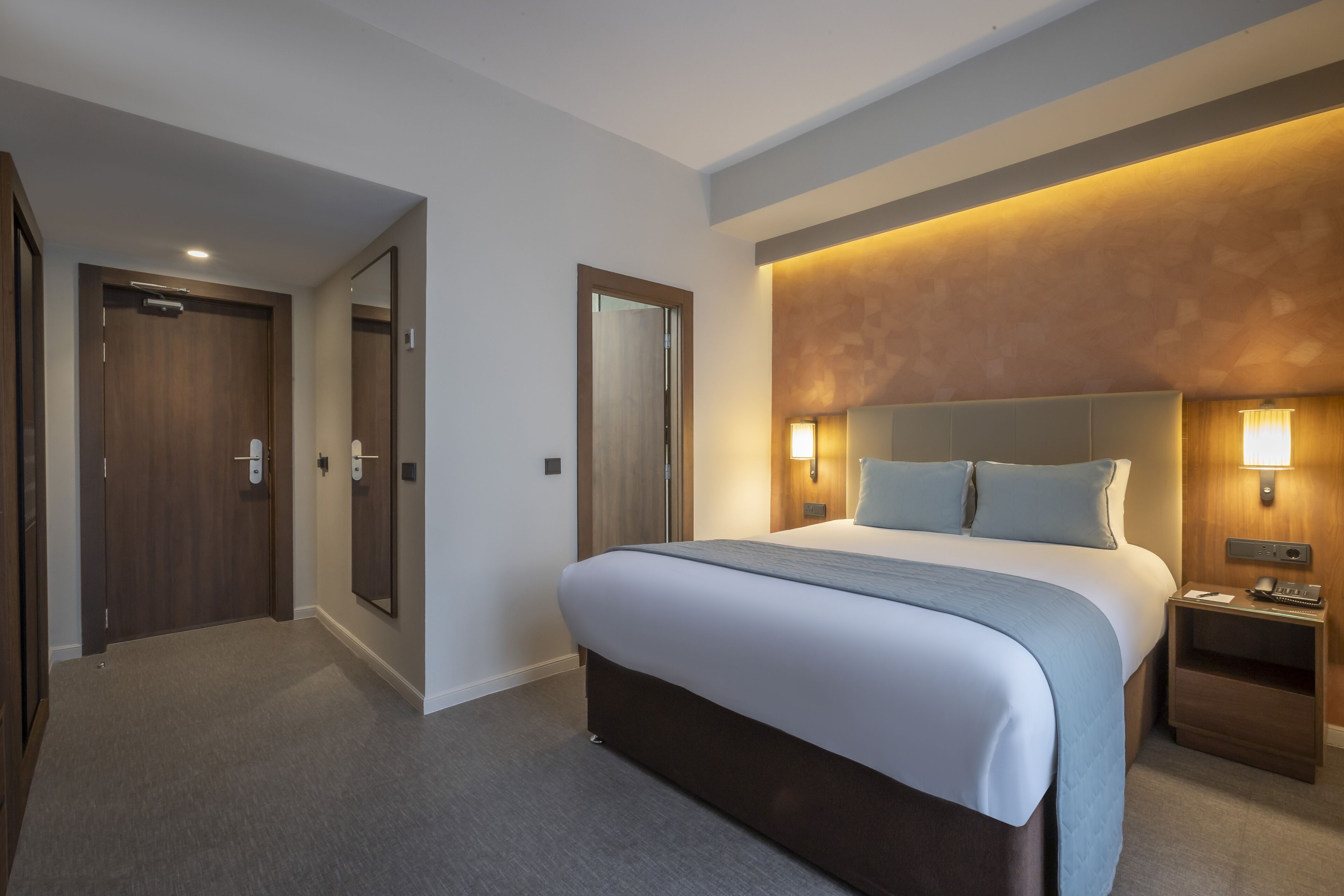 A hotel room with a large bed, a nightstand, a mirror, and a door.