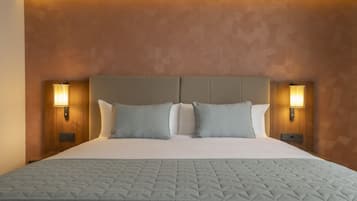Una cama grande con cubrecolcha acolchado, dos lámparas fijadas a la pared y una pared texturizada detrás de la cama.
