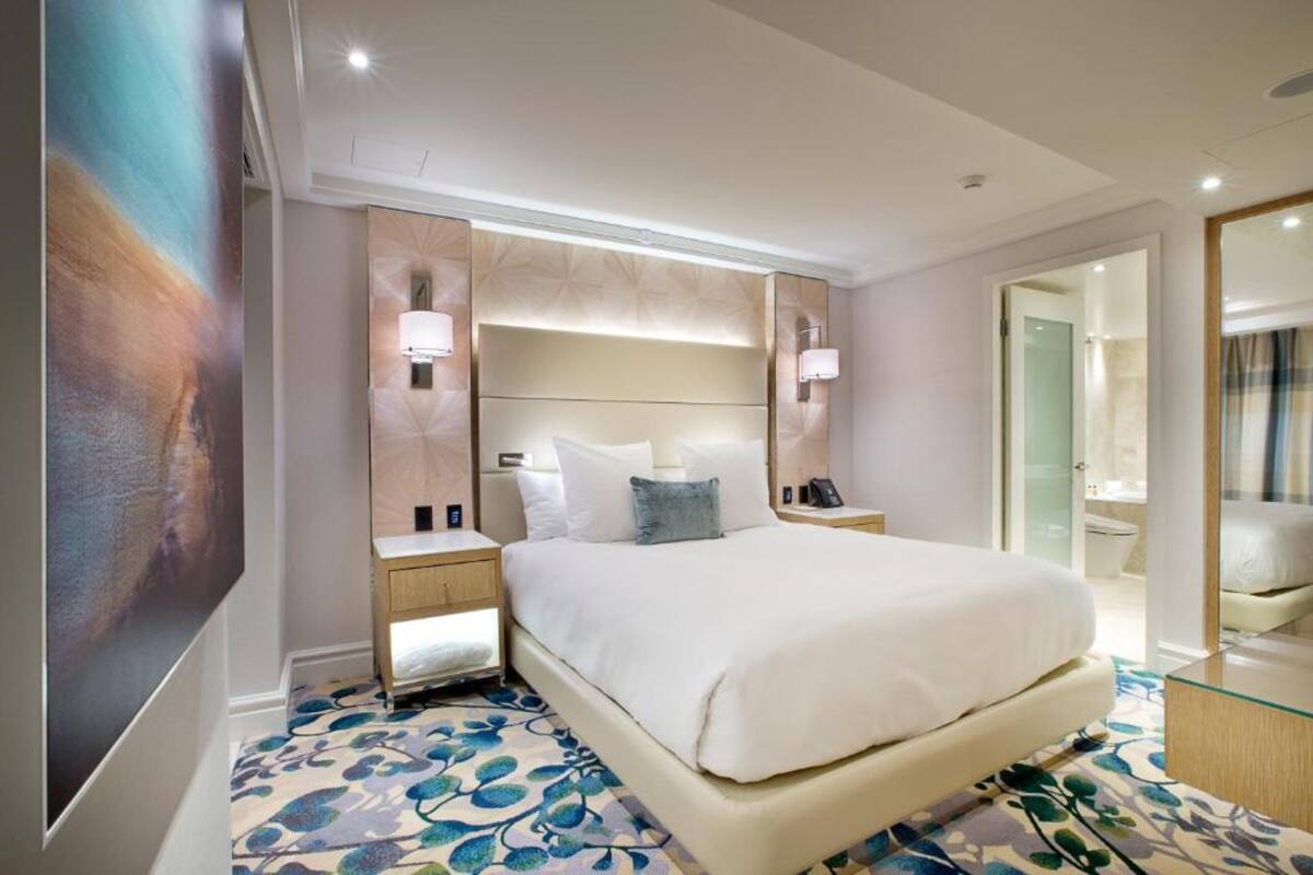 Une chambre d’hôtel moderne avec un grand lit, des lampes de chevet, un miroir et une cloison en verre.