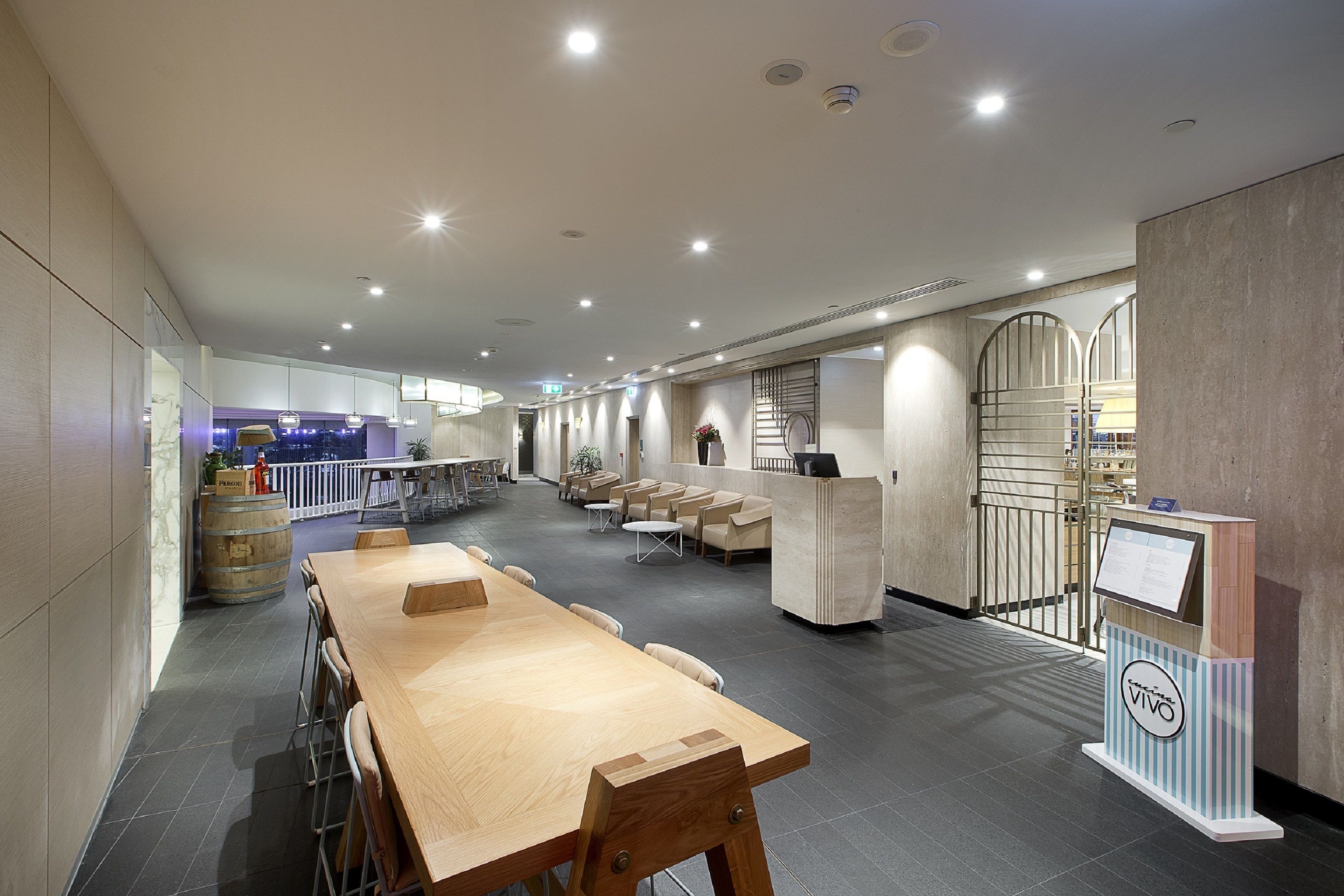 A spacious indoor area with a long wooden table, several chairs, a reception desk, and a staircase leading to an upper level.