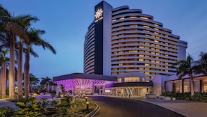 A modern hotel with a curved facade, a prominent star logo, and a well-lit entrance area with palm trees and plants.