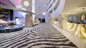 A modern hotel lobby with a zebra-striped carpet, a reception desk, and a seating area with a sofa and a table.