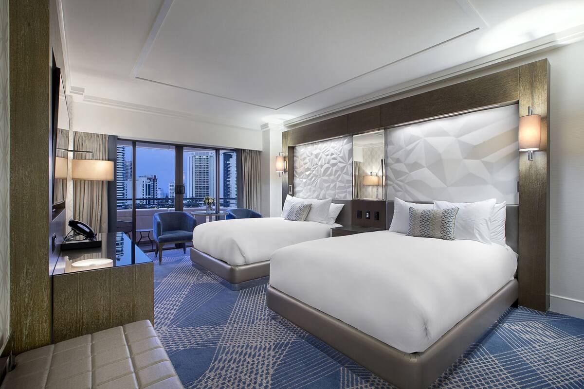 Une chambre d’hôtel moderne avec deux lits, un coin salon offrant une vue sur la ville et une grande fenêtre.