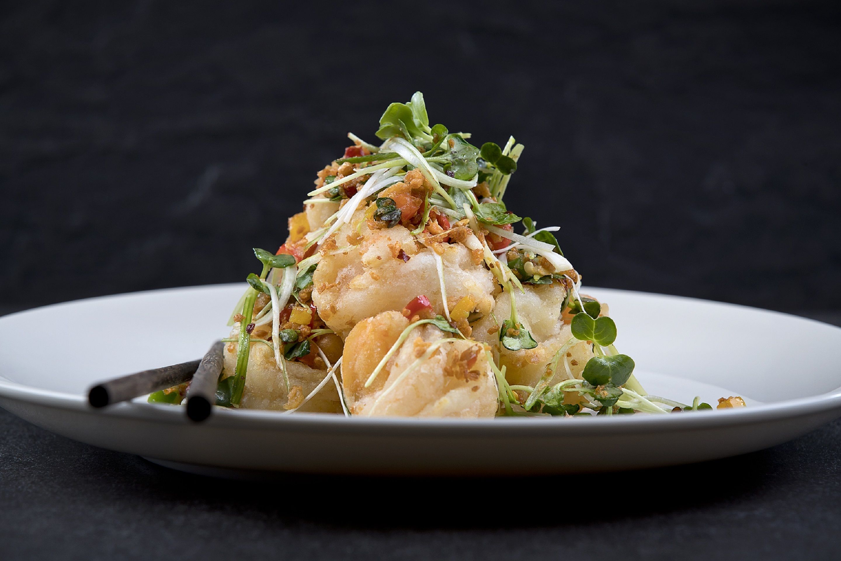 A white plate with a seafood dish garnished with greens and red peppers.