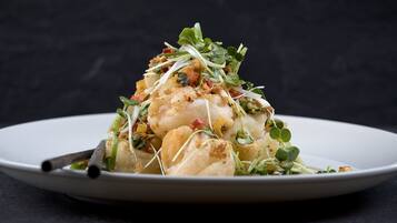 A white plate with a seafood dish garnished with greens and red peppers.