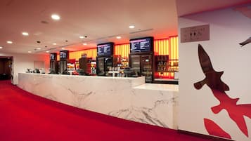 Zona de recepción de un hotel con mostrador de mármol, pantallas digitales con menú y alfombra roja.