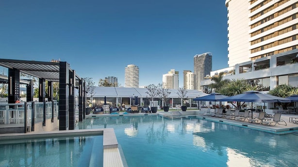 A swimming pool with lounge chairs and umbrellas, surrounded by high-rise buildings.