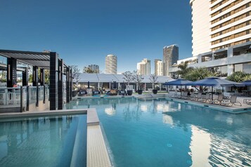 Una piscina al aire libre, sombrillas, sillones reclinables de piscina