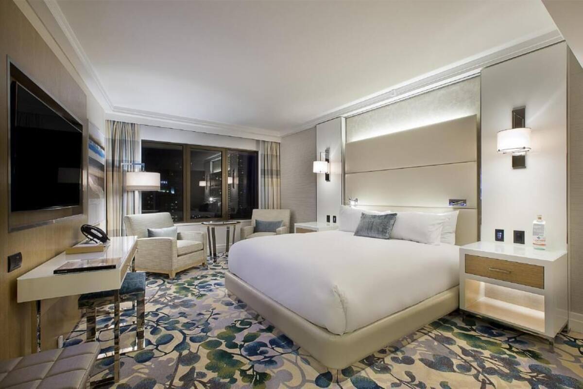 Une chambre d’hôtel avec un grand lit, un bureau avec une chaise, une petite table, une table de chevet et un grand miroir.
