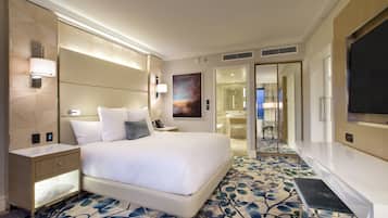 Una habitación de hotel moderna con una cama grande, mesitas de noche, un televisor de pantalla plana y un baño visible a través de una puerta abierta.