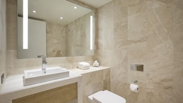 Un baño moderno con un lavamanos rectangular, un espejo, un inodoro y un dispensador de toallas.
