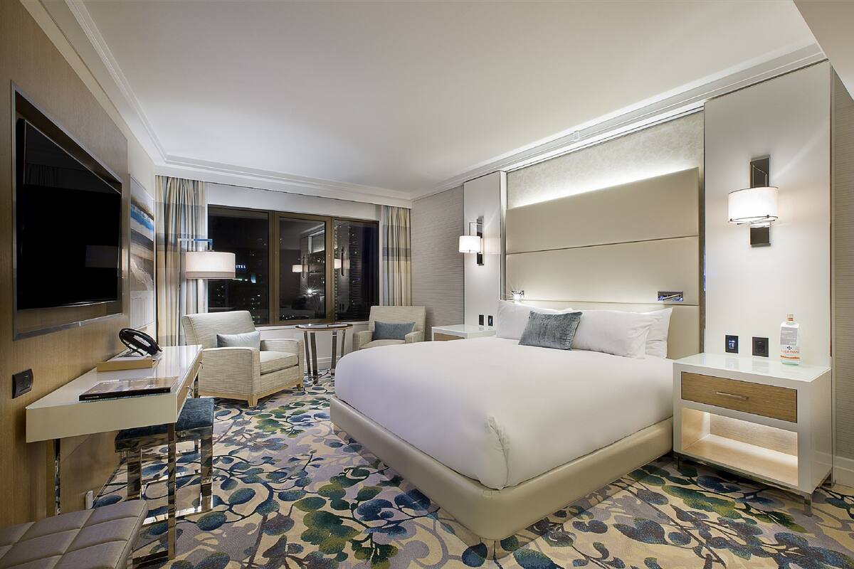 Une chambre d’hôtel avec un grand lit, un bureau avec une chaise, une petite table, une table de chevet et un grand miroir.
