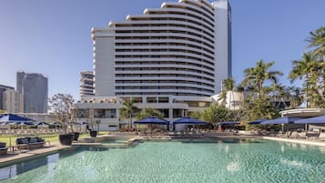A hotel with a large pool, sun loungers, and palm trees.
