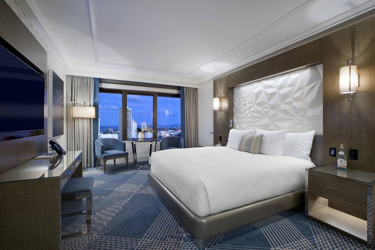 Une chambre d’hôtel moderne dotée d’un grand lit, d’un bureau avec une chaise, d’une télévision et offrant une vue sur la ville.