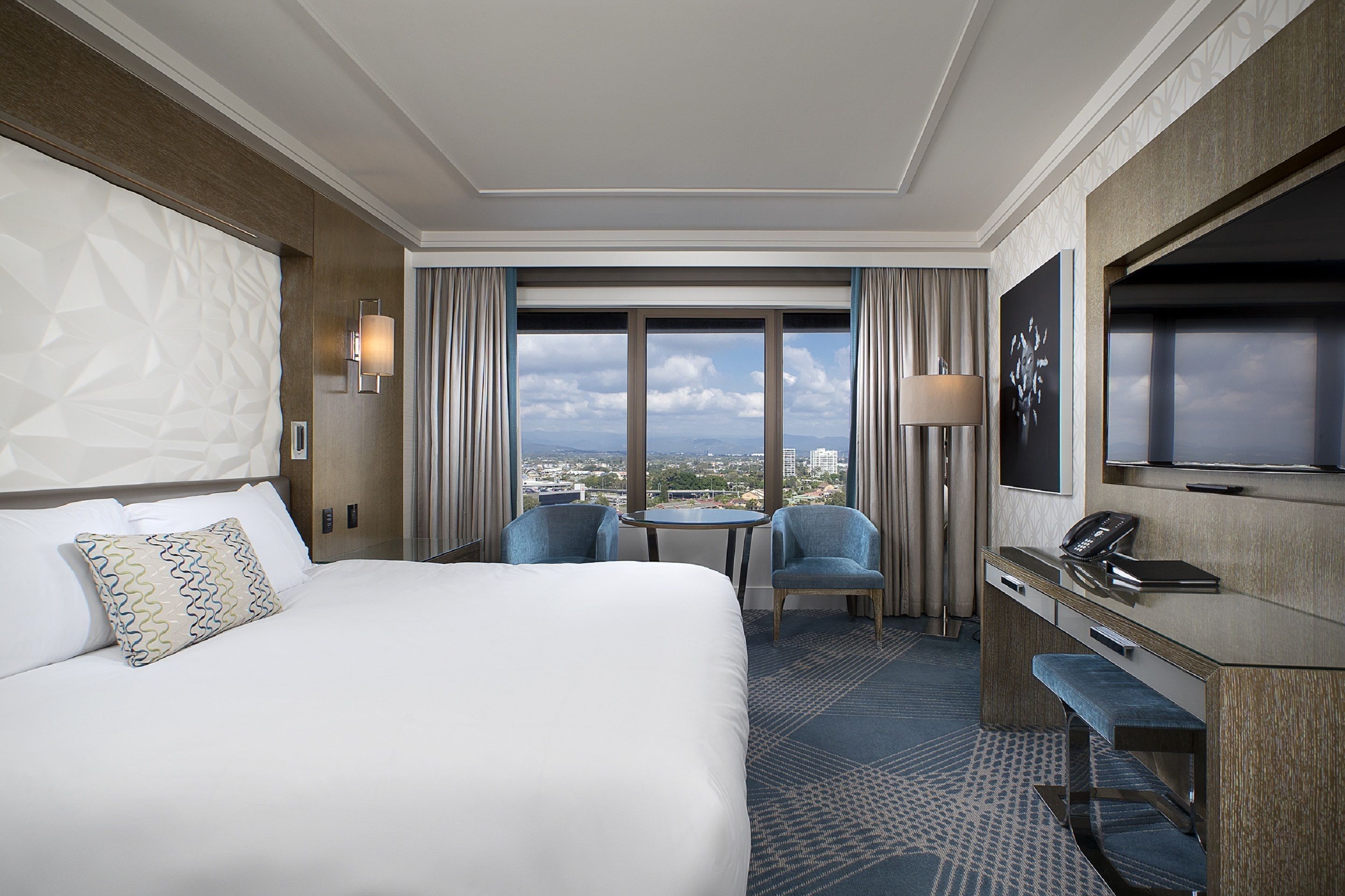 A hotel room with a large bed, a desk with a telephone, two chairs, a small table, and a TV.