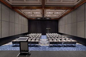 Un salón de conferencias con filas de mesas y sillas, un atril y una alfombra estampada.