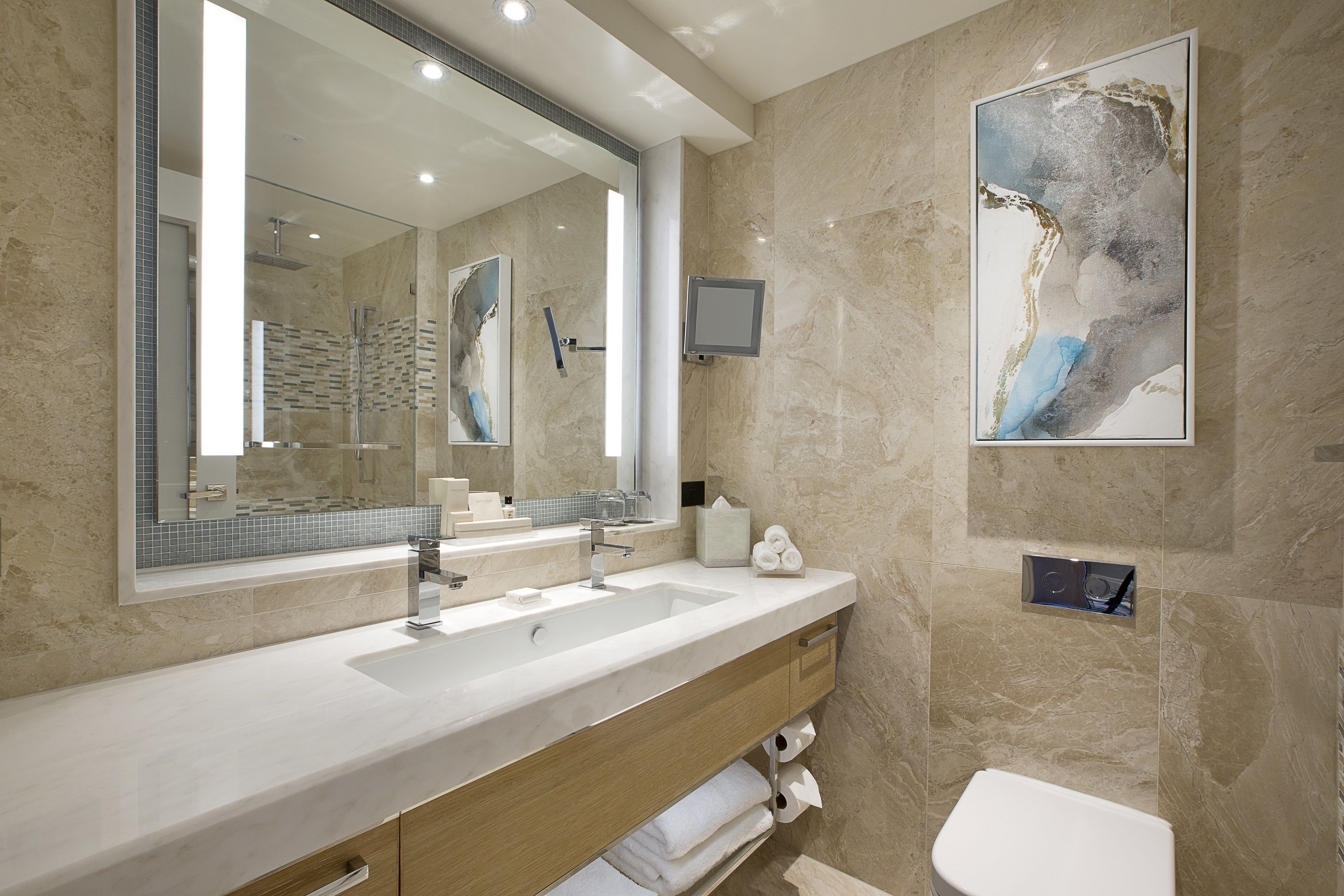 A modern bathroom with a large mirror, two sinks, a toilet, and a shower.