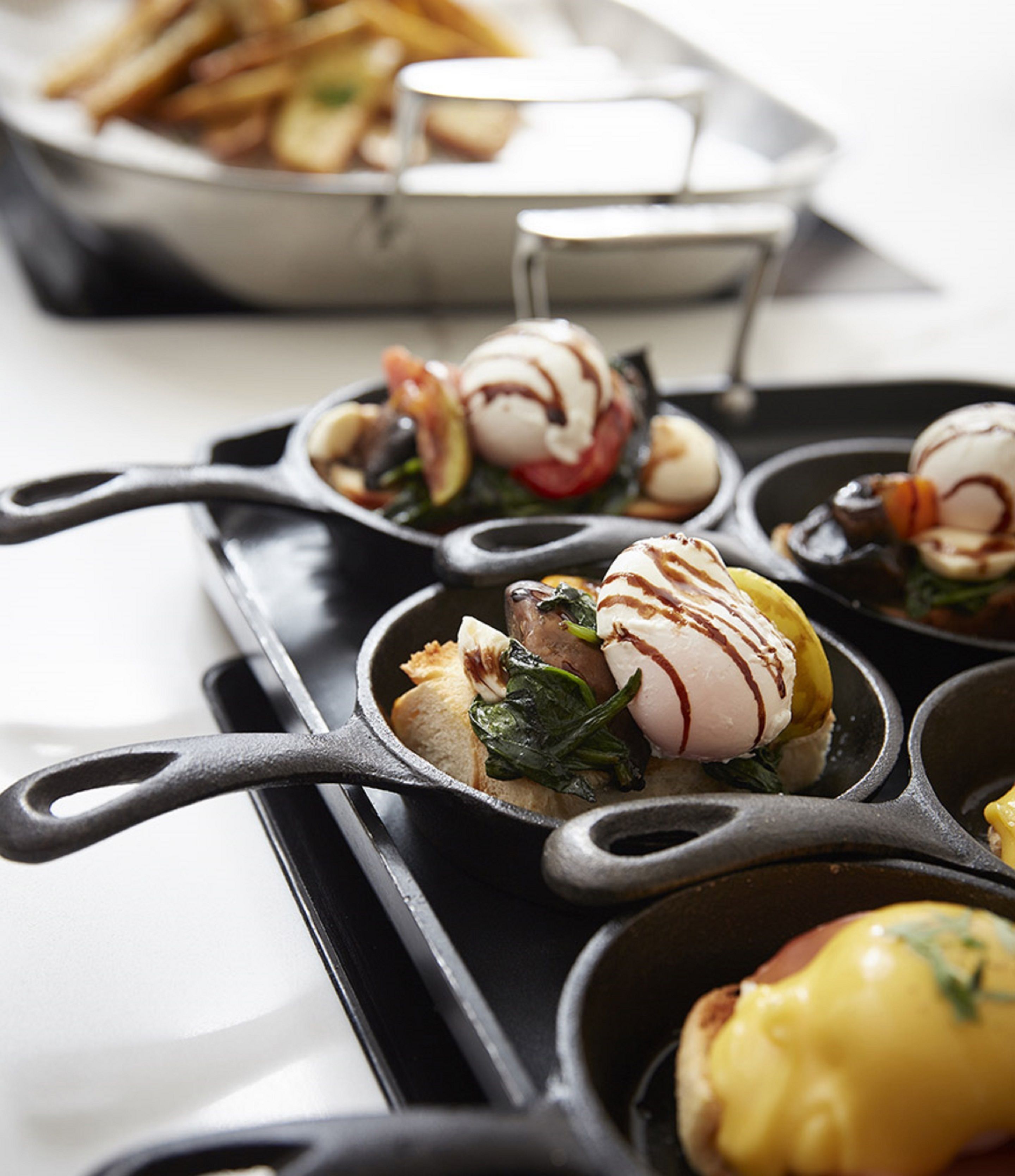 A kitchen with a cast iron skillet containing food, a tray with fries, and a bowl of soup.