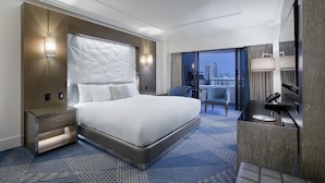A modern hotel room with a large bed, bedside tables, a desk, and a city view.