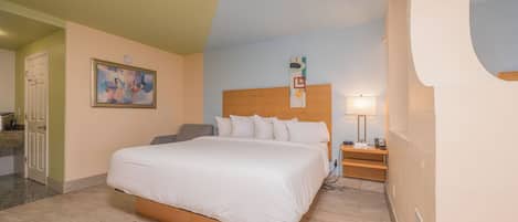 A hotel room with a large bed, a bedside table with a lamp, a painting on the wall, and a door to the left.