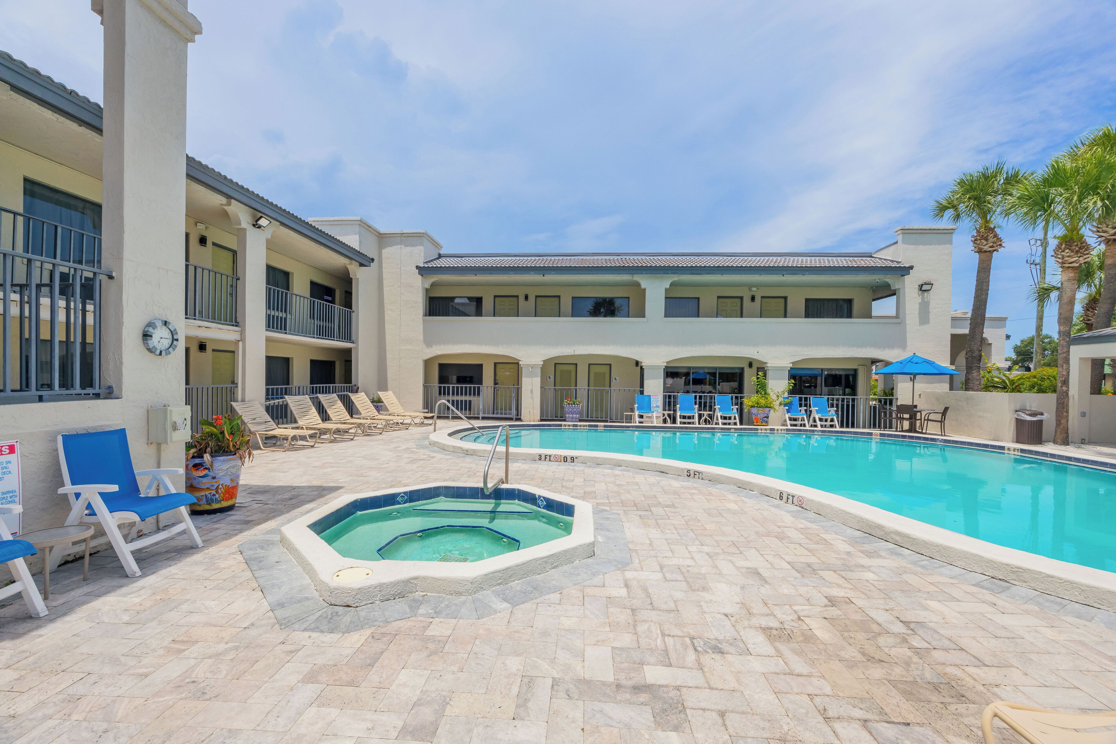 A pool area with lounge chairs, a hot tub, and a multi-story building with balconies.