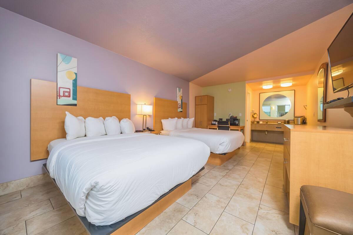 A hotel room with two beds, a desk, a mirror, and a bathroom.