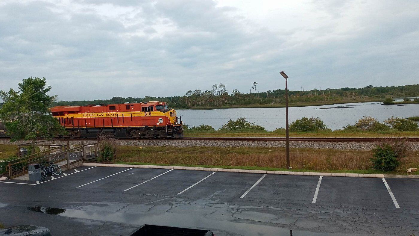 A train on tracks near a body of water, with a parking lot in the foreground.