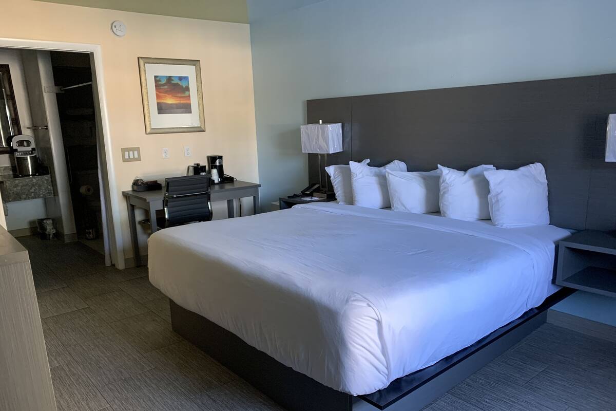 A hotel room with a large bed, a desk with a chair, a lamp, and a painting on the wall.