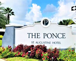 Placa do The Ponce St. Augustine Hotel com um logotipo circular, rodeada por jardins bem cuidados.